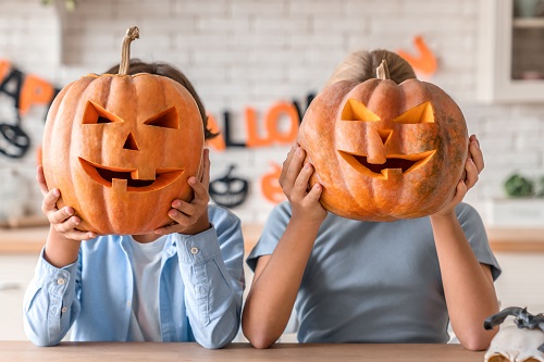 duas crianças segurando uma abóbora decorada de halloween