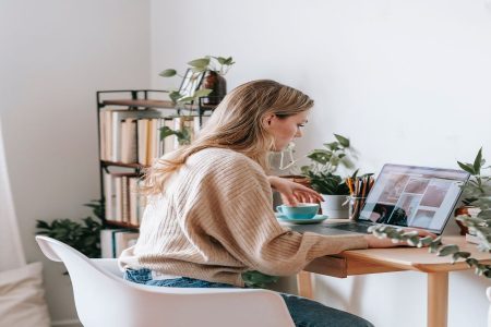 mulher sentada em frente ao computador trabalhando, tomando uma xícara de chá