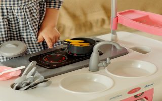 menina brincando com uma cozinha infantil de plástico nas cores rosa e branco