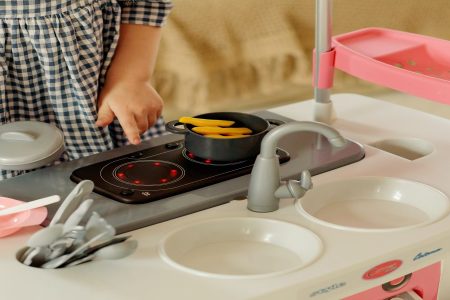 menina brincando com uma cozinha infantil de plástico nas cores rosa e branco