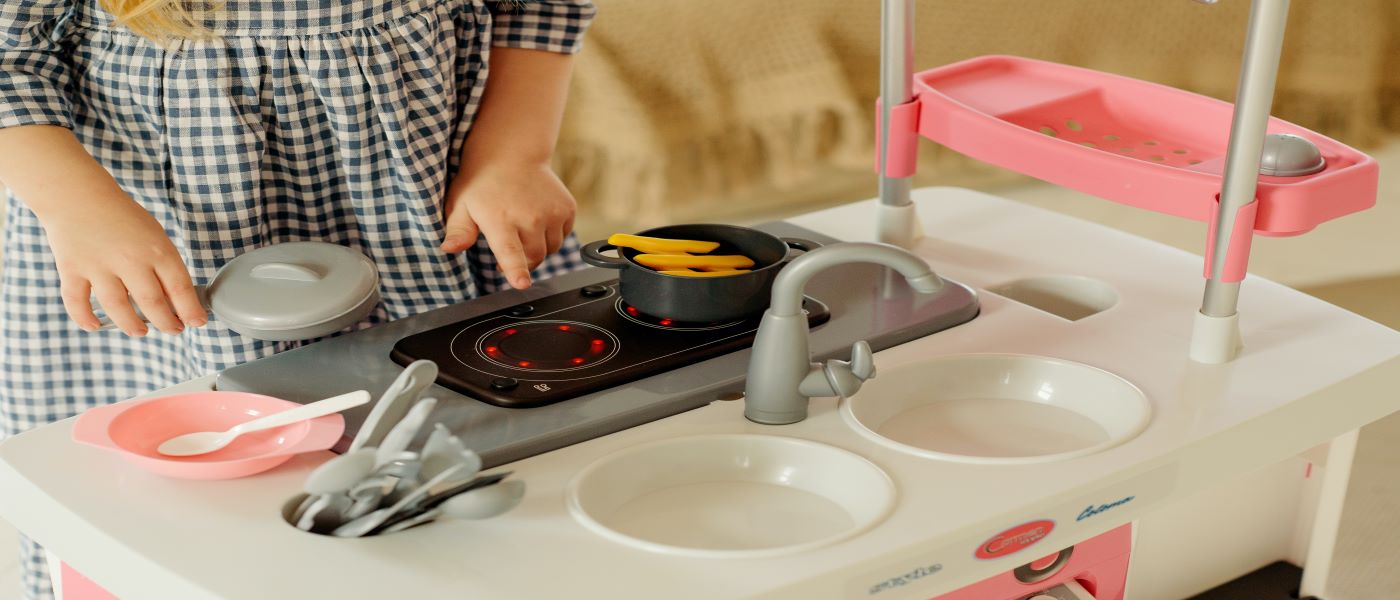 menina brincando com uma cozinha infantil de plástico nas cores rosa e branco