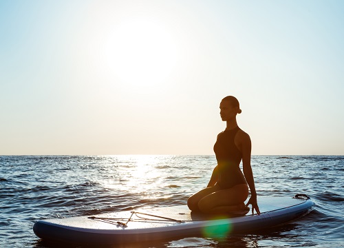 mulher praticando yoga em cima de uma prancha de paddle surf 