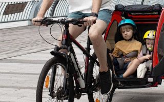 duas crianças dentro de um reboque de bicicleta infantil sendo puxadas pela bicicleta do pai