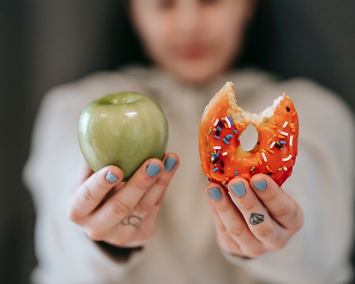 alimentação saudável, mulher ensinado uma maça e um donnuts 