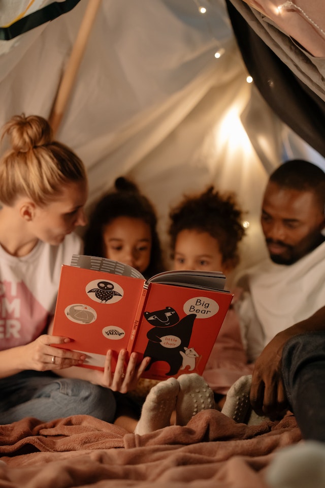 pais lendo um livro para as crianças antes de irem dormir