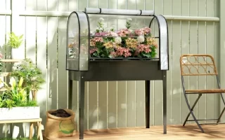 Floreira elevada com cobertura transparente, rodeada de plantas e flores num terraço de madeira.